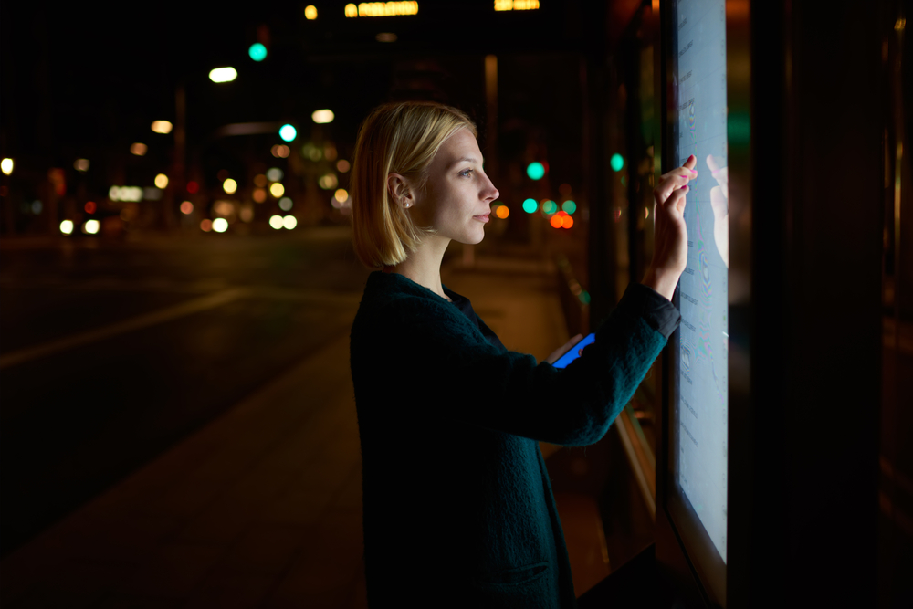 Uma mulher interagindo com um totem eletrônico em um ponto de ônibus.