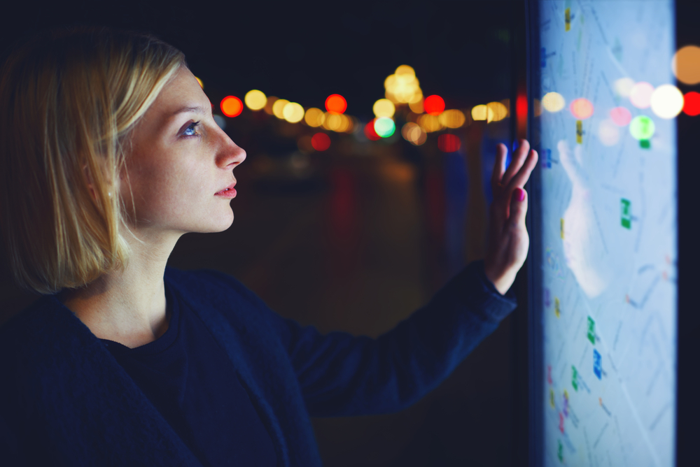 Uma mulher observa em um painel digital, posicionado na rua, um mapa para se localizar.